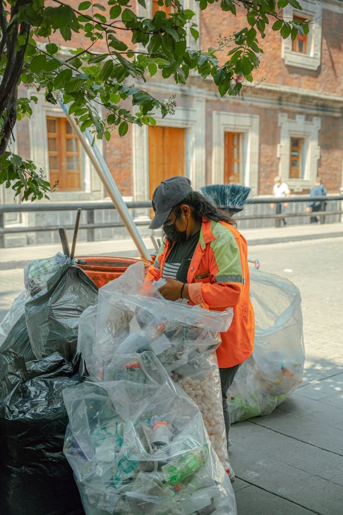 A worker sorting plastic bottles for recycling on a sunny city street.